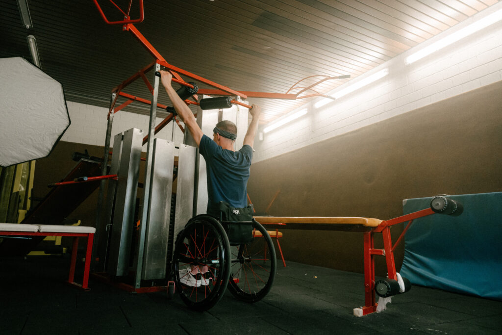 A paralympic athlete in a wheelchair performing strength training exercises in a gym, with professional lighting setup for capturing high-quality footage for video editing.